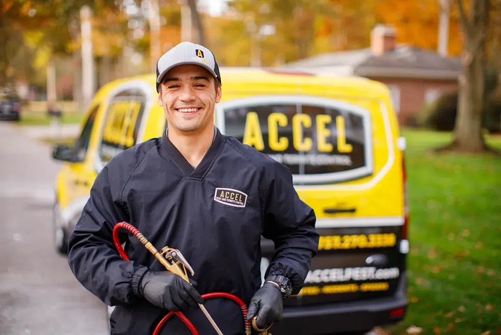 Accel Pest employee holding equipment in front of work van.