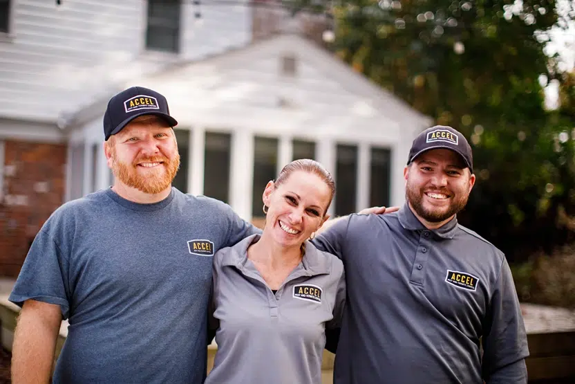 Three uniformed pest control professionals from Accel stand together smiling outside a house.