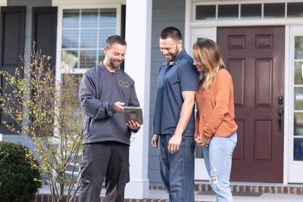 An exterminator works alongside a family couple outside their front door.