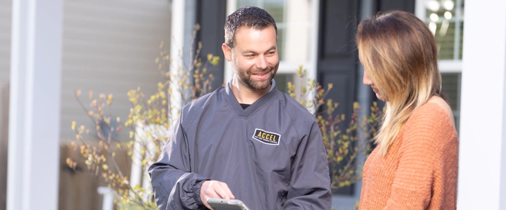 An Accel Pest exterminator works alongside a woman outside her home.
