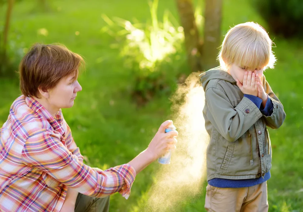 Woman spraying insect or mosquito repellents on little boy before a walk in the forest. Protect children from mosquitoes and other insects. Summer activities for family with child, hiking.